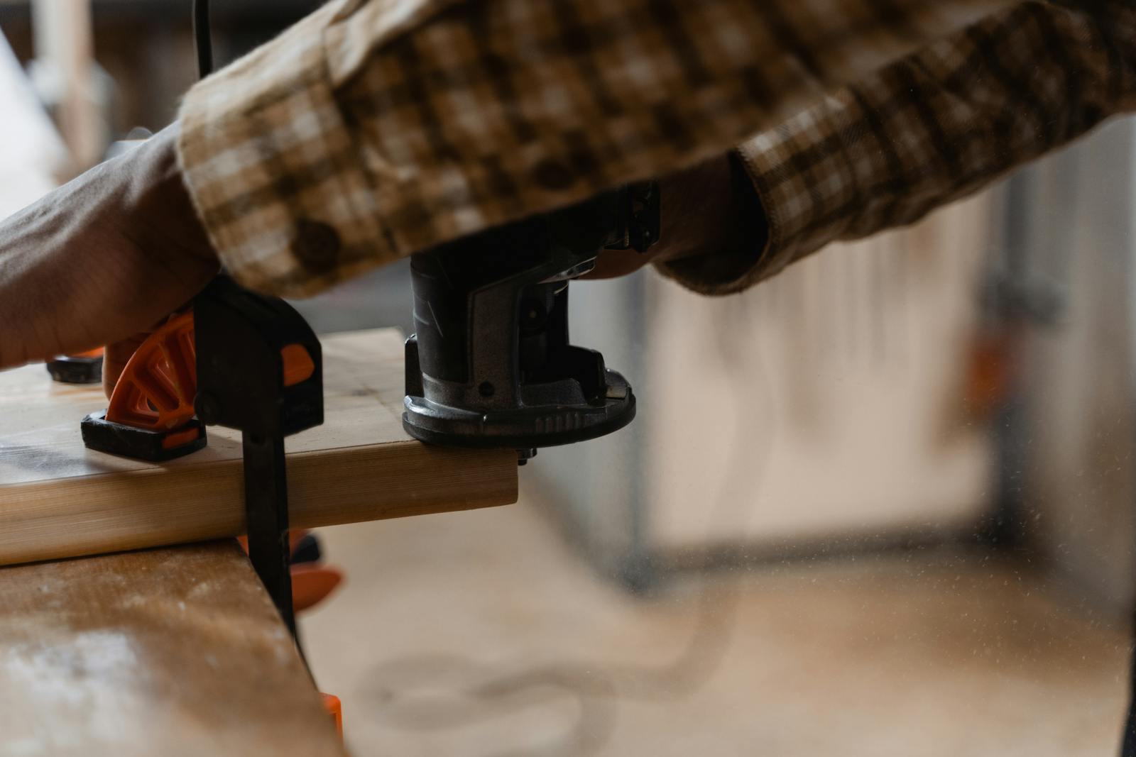 A carpenter works with an electric router on wood indoors, showcasing craftsmanship.