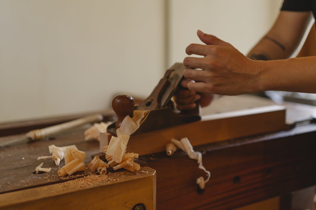 Crop joiner shaping hardwood plank with jack plane working at table in modern workshop