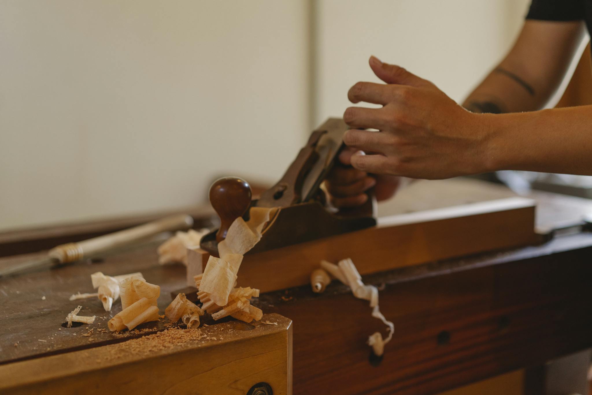 Crop joiner shaping hardwood plank with jack plane working at table in modern workshop